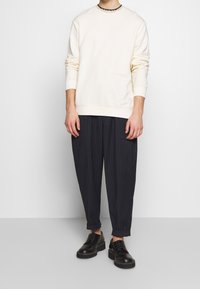 Felpa beige chiaro con maniche lunghe, polsini a costine, abbinata a pantaloni tapered a righe scure e scarpe nere con lacci.