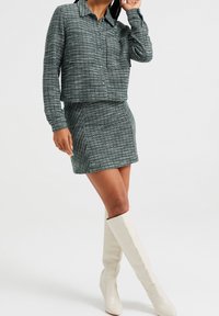 Conjunto de dos piezas a cuadros verdes que incluye una camisa de manga larga con cuello y una minifalda ajustada, combinados con botas altas blancas hasta la rodilla.