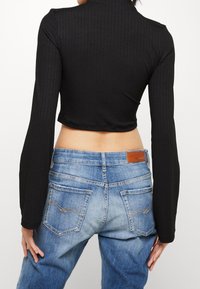 Musta ribbattu pitkähihainen crop-top, joka on yhdistetty vaaleansinisiin farkkuihin, joissa on taskut ja ruskea nahkapatch vyötärölinjalla.