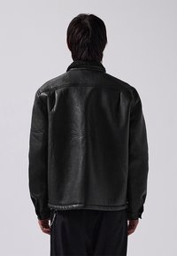 Black leather jacket featuring a shearling collar, structured shoulders, and a relaxed fit. Smooth texture with visible stitching details.