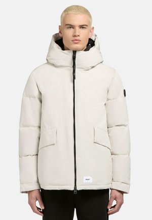 Lyse beige polstret jakke med høj krave, lynlås lukning, forlommer og aftagelig hætte. Har en sort foring og logo accent.