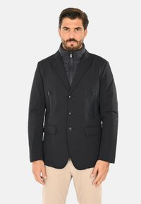 Giacca blazer nera con collo con cerniera, tessuto liscio, bottoni frontali e due tasche al petto con zip; vestibilità sartoriale con tasche laterali.
