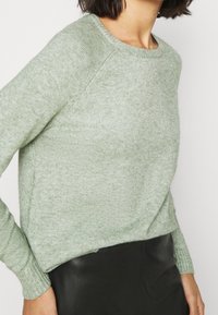 Ljusgrön tröja gjort av ett mjukt, strukturerat material. Har rund halsringning och ribbade ärmmuddar. Kombineras med en svart läderkjol.