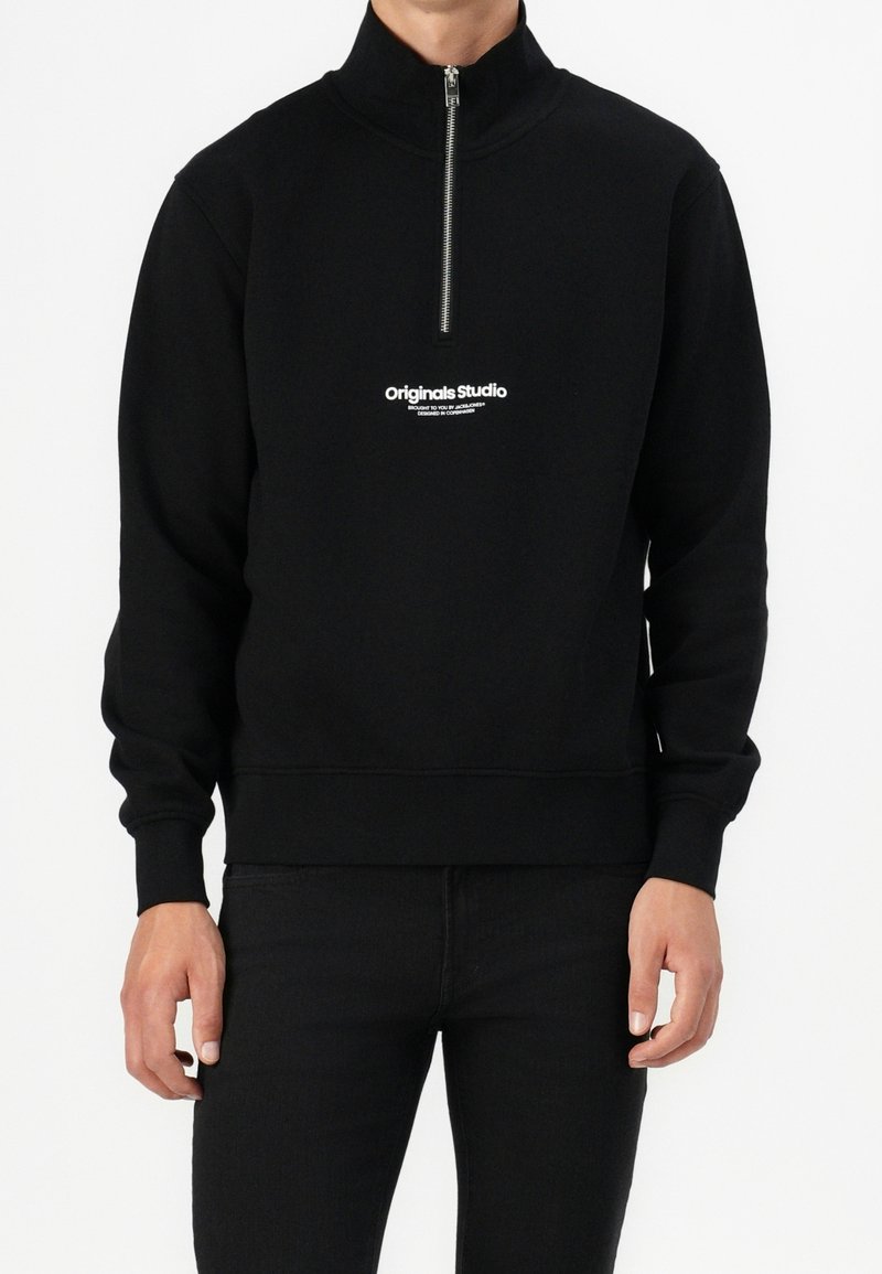 Czarna bluza zapinana na zamek, wykonana z miękkiego materiału, z wysokim kołnierzem i białym logo na piersi. Dopasowany krój z prążkowanymi mankietami.