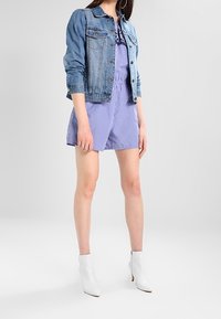 Jeansjacka med ljusblå tvätt och figurnära design. Under finns en randig sparkdräkt i blått och vitt. Vita ankelstövlar fulländar looken.