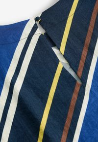 Tissu rayé comportant des couleurs bleue, blanche, jaune et marron. Le design inclut un col et une fermeture à bouton avec une coupe diagonale.