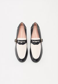 Black and white leather loafers with a rounded toe, featuring a black strap and gold buckle across the instep and a smooth, shiny texture.