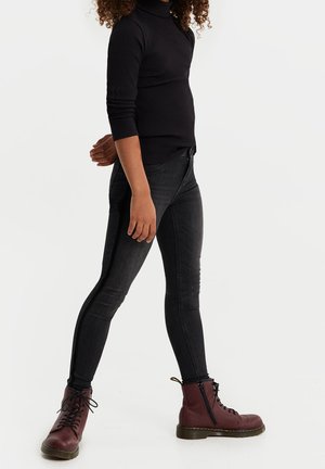 Czarny prążkowany golf zestawiony z dopasowanymi ciemnoszarymi dżinsami. Model nosi bordowe sznurowane botki z kontrastową podeszwą i zamkiem bocznym.