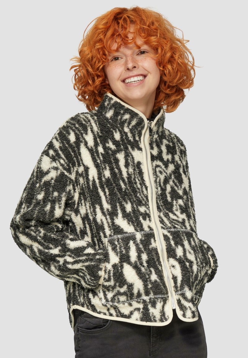 Zwarte en crèmekleurige fleece jas met patroon, hoge kraag, ritsluiting en twee voorkruiken. Zachte textuur en een relaxte pasvorm.