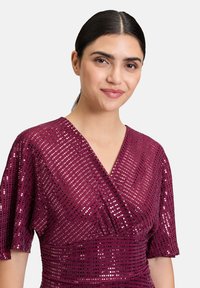 Burgundowa sukienka z zapięciem, z krótkimi rękawami i teksturowaną powierzchnią z cekinów o różnych rozmiarach i wzorach.