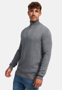 Pulover tricotat gri cu guler înalt, având un model în zigzag, mâneci lungi și un închideri cu fermoar la gât. Textură moale, design ajustat.
