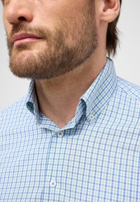 Camicia a quadri blu e verde con colletto classico, pattina con bottoni corta e tessuto testurizzato con una leggera lucentezza.