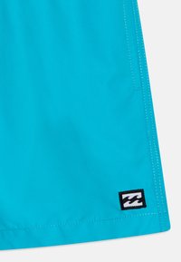 Bright blue fabric with double-stitched hem and small black-and-white wave logo patch near the bottom edge.