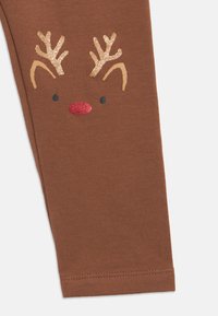 Καφέ παντελόνι από ύφασμα με το πρόσωπο ενός λαμπερού ελαφιού που δείχνει χρυσά κέρατα, μπεζ αυτιά, μαύρα μάτια και κόκκινη μύτη.