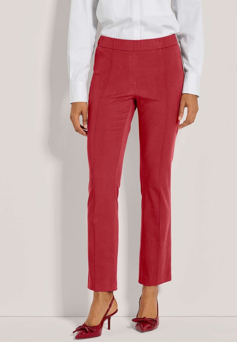 Rote Slim-Fit-Hosen mit mittelhohem Bund, strukturiertem Stoff, Seitennähten und kombiniert mit glänzenden roten High Heels.