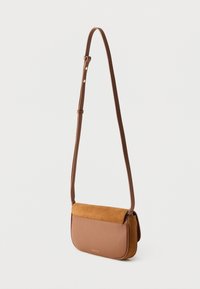 Brūna ādas plecu soma ar zamšādas pārsegu, tai ir gluda tekstūra un regulējams siksnas garums, kompakts dizains ar smalkiem zelta akcentiem.