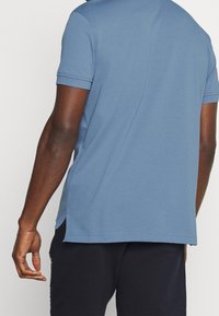 Blå bomullspikétröja med avslappnad passform, med korta ärmar, rundad nederkant och sidoflikar för ökad komfort.