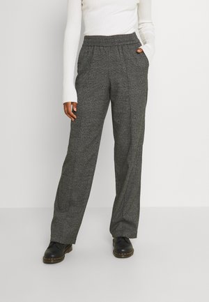 Šedé kostkované kalhoty s širokými nohavicemi, elastickým pasem a bočními kapsami, vyrobené z texturované látky. Černé boty doplňují celý outfit.