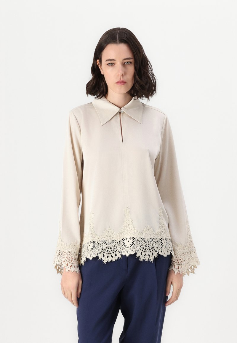 Blusa beige con colletto, scollo a chiave e maniche lunghe. Bordo e polsini con dettagli in pizzo. Tessuto morbido, vestibilità ampia.
