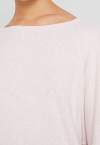 Helles rosa Sweatshirt mit weicher Textur und Bootsausschnitt, ausgestattet mit kurzen Ärmeln und minimalen Nähdetails, die ein entspanntes Design betonen.