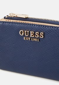 Navy blue textured wallet made of synthetic material, featuring a gold-tone logo and zipper closure. Smooth accents with a subtle pattern.