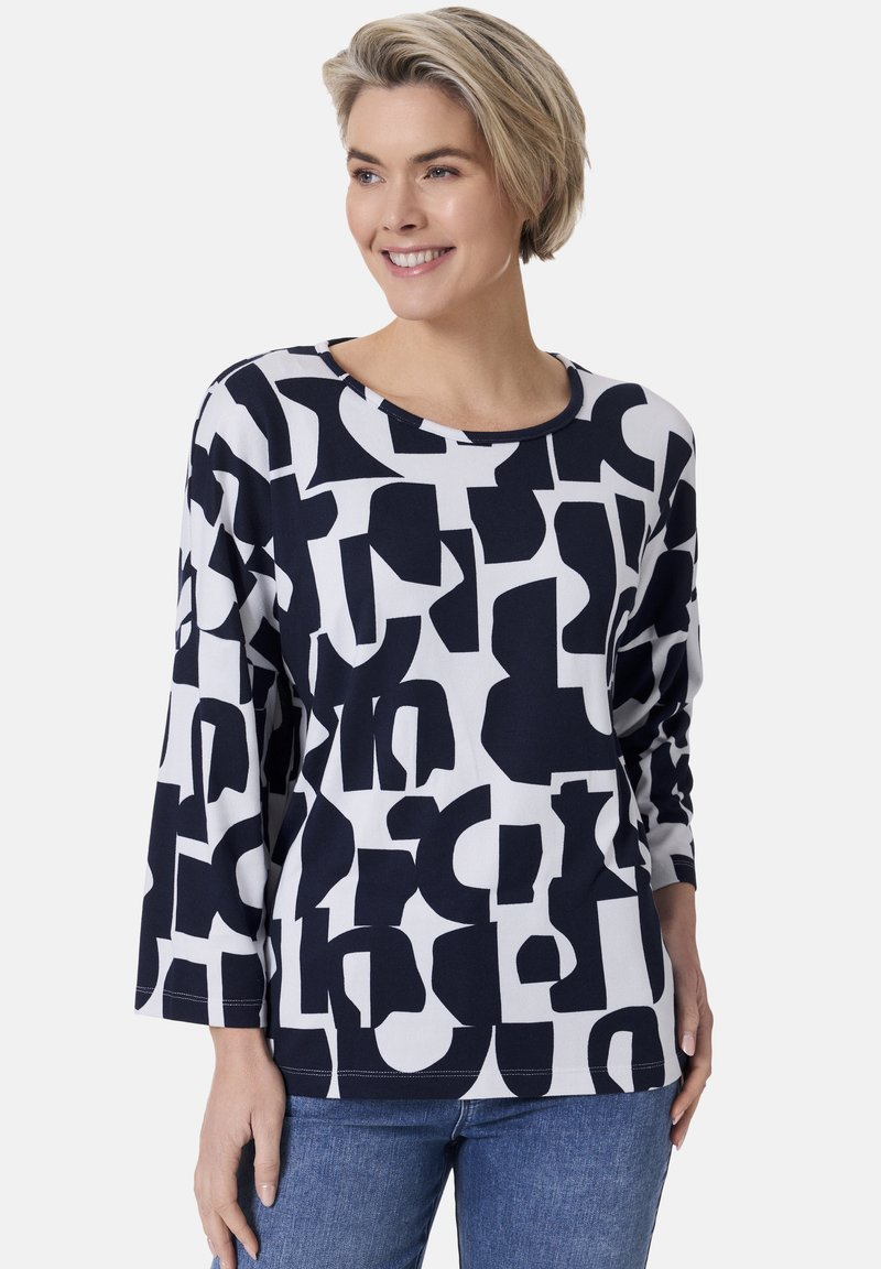 Langärmliges Oberteil aus weichem Stoff, mit einem auffälligen schwarz-weißen grafischen Muster, rundem Halsausschnitt und legerer Passform. Kombiniert mit Jeans.