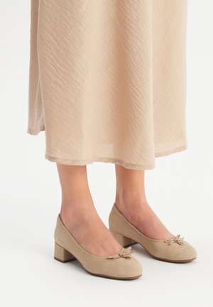 Beige nubuck kengät, joissa on matalat korot, pyöristetyt varpaat ja koristeelliset nauhat etuosassa. Yksinkertainen muotoilu, sileä pinta ja tukeva muoto.