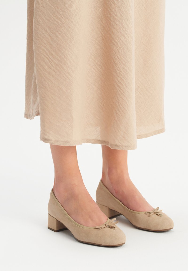 Beige nubuck kengät, joissa on matalat korot, pyöristetyt varpaat ja koristeelliset nauhat etuosassa. Yksinkertainen muotoilu, sileä pinta ja tukeva muoto.