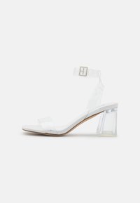 Sandales à talons transparents avec une semelle blanche, des sangles transparentes, une boucle à la cheville et un talon bloc avec un design géométrique.