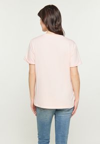 Ljusrosa t-shirt med kort ärm och avslappnad passform, rundad halsringning och uppvikta ärmar, kombinerat med blå jeans. Slät textur.