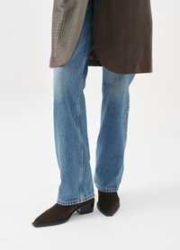 Cappotto marrone con motivo coccodrillo e orlo curvo, abbinato a jeans dritti blu chiaro e stivaletti alla caviglia marroni scuri a punta.