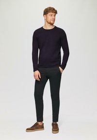 Donkerpaarse langemouwen shirt, zwarte slim-fit broek, bruine suède sneakers met rubberen zolen, staande op een lichte achtergrond.