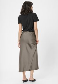Sorte t-shirt og olivengrøn satin midi-nederdel med elastisk talje, glat tekstur og enkel design; modellen har sorte hæle mules på.