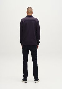 Sudadera morada con cuello, mangas largas y corte recto, combinada con jeans oscuros y zapatillas negras. Vista trasera.