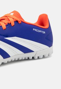 Scarpa da calcio blu con accenti arancioni, tomaia sintetica texturizzata, strisce bianche e suola in gomma modellata per una buona aderenza. Marchio visibile di lato.
