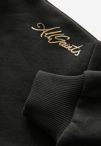 Sudadera negra con puños acanalados. Tejido texturizado con un acabado suave. Destacado detalle del logo dorado a lo largo del hombro.