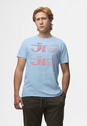 Světle modré bavlněné tričko s vybledlým vícebarevným grafickým textem, na kterém je nápis "JT Racing USA" v červené, růžové a zelené barvě.