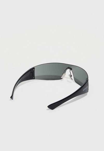 Aurinkolasit, joissa on tyylikäs musta muovirunko, kaarevat harmaat linssit ja brändäys sankassa. Sisältää säädettävät nenätyynyt.