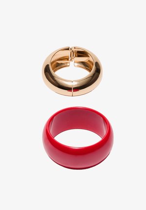 Dvě masivní náramky na bílém pozadí; jeden lesklý zlatý s pantovým zapínáním, druhý hladký červený náramek bez otevírání.