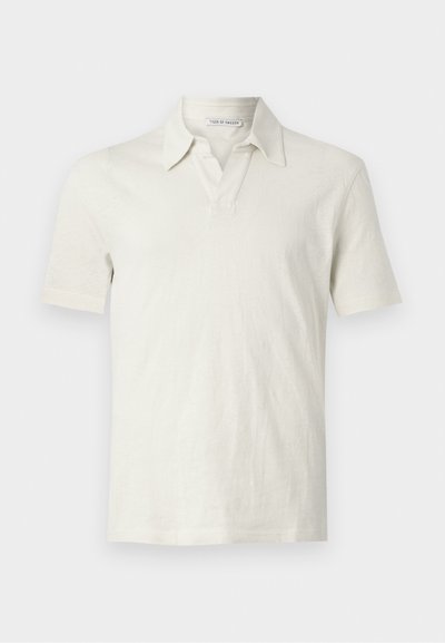 Polo de color beige claro en un tejido suave y texturizado. Cuenta con un cuello clásico y una botonera parcial. Manga corta con un corte relajado.