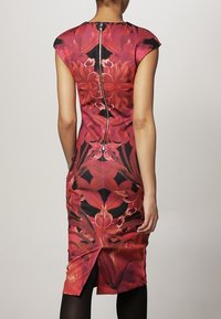 Robe moulante avec un imprimé floral vibrant en rouge et noir, manches courtes et fermeture éclair au dos. Texture lisse, longueur genou.