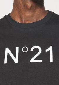 Musta puuvillatee paita, jossa on suuri valkoinen printti "N°21" edessä. Kangas näyttää sileältä ja siinä on tavallinen pyöreä kaula-aukko.