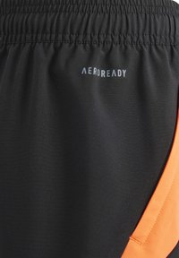 Zwarte sportshorts met een elastische tailleband, voorzien van een opvallend oranje zijpaneel en het "AEROREADY" logo in het grijs op de stof.