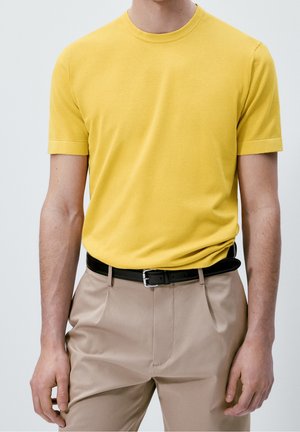 Yellow cotton t-shirt with a round neckline and short sleeves, paired with beige trousers and a black belt. Simple, textured design.