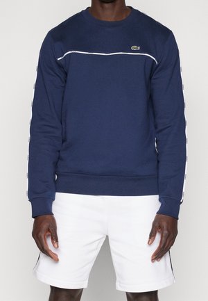 Marineblaue Sweatshirt aus Baumwollmischung, mit einem weißen horizontalen Streifen und Logo auf der Brust sowie gebrandeten Akzenten entlang der Ärmel.