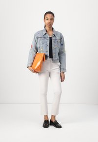 Jeansjacka med blomsterbroderi, svart topp, vita cropped byxor, håller en orange kuvertväska och svarta loafers. Enkel, modern design.