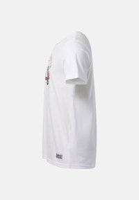 T-shirt blanc à manches courtes, vue latérale montrant un imprimé graphique sur la poitrine et un petit patch rectangulaire près de l'ourlet.
