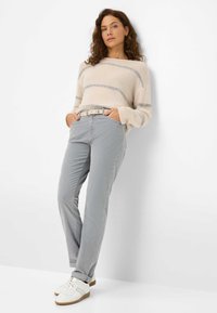 Beige und grau gestreifter Pullover, hellgraue Hose mit einem Gürtel und weiße Sneaker. Lässig, weicher Stoff mit lockerer Passform und geraden Beinen.