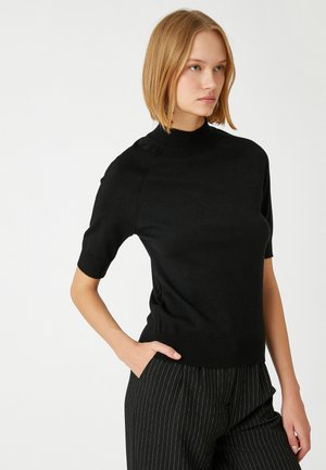 Zwarte trui met korte mouwen en een hoge hals. Heeft een aansluitend ontwerp, een gladde textuur en een ribbelrand. Gemanipuleerd met gestreepte broek.