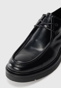 Zapato de cuero negro con puntera redondeada, superficie lisa, costuras sutiles y suela de goma. Presenta cordones finos y un diseño elegante.